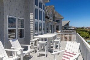 A wooden deck with white furniture, including chairs and tables, overlooking a residential area. - Sea Forevermore: Oceanside, Private Pool, 2 Hot Tubs, Elevator (Corolla)