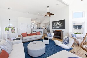 A spacious living room with a grey sofa, ottoman, and striped armchairs, a ceiling fan, and a kitchen in the background. - Sea Forevermore: Oceanside, Private Pool, 2 Hot Tubs, Elevator (Corolla)