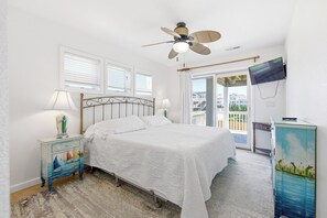 Une chambre à coucher avec un lit, un ventilateur de plafond, une télévision et une vue sur l’extérieur.