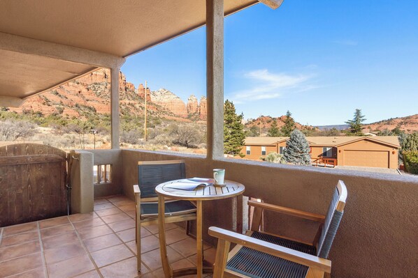 A balcony with a view of red rock formations, a wooden table with chairs, and a hot tub.
