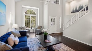 A spacious living room with a blue sofa, a coffee table, and a large window. - Serene, Stylish, and Spacious 3BD 2BA House Near Wineries (Sonoma)