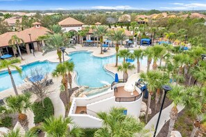 Een resort met een groot zwembad, palmbomen en terrasjes.