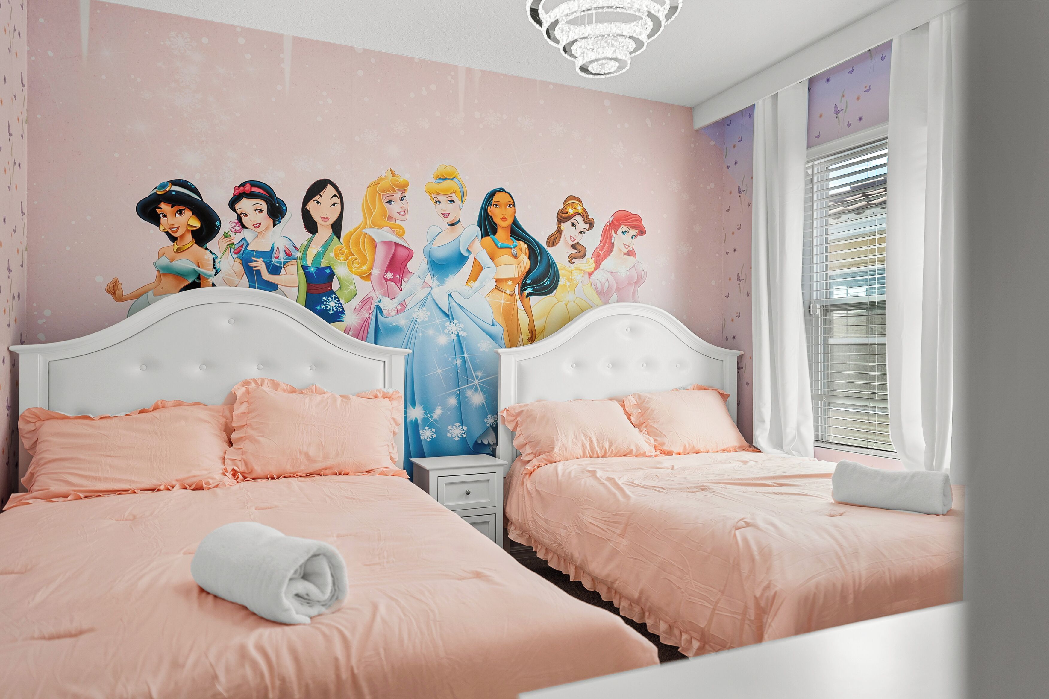 A bedroom with two beds, pink bedding, and a wall mural of Disney princesses.