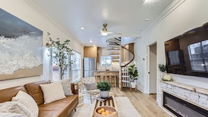A modern living room with a brown leather sofa, a fireplace, and a kitchen area with a spiral staircase.