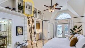 Une chambre avec un grand lit, un ventilateur de plafond, une échelle, une salle de bain et une vue sur l’extérieur.