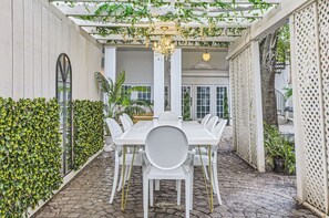 A covered patio with a white table and chairs, surrounded by greenery and a decorative ceiling. - Secret oasis in the heart of Montrose, outdoor dining, firepit, gazebo and grill (Houston)