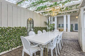 A covered patio with a white table and chairs, surrounded by greenery and a decorative ceiling. - Secret oasis in the heart of Montrose, outdoor dining, firepit, gazebo and grill (Houston)