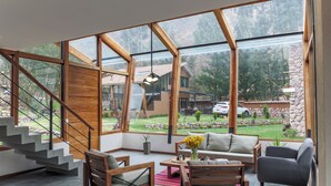 Amplia sala de estar con un gran muro de cristal, una escalera de madera y vistas al exterior.