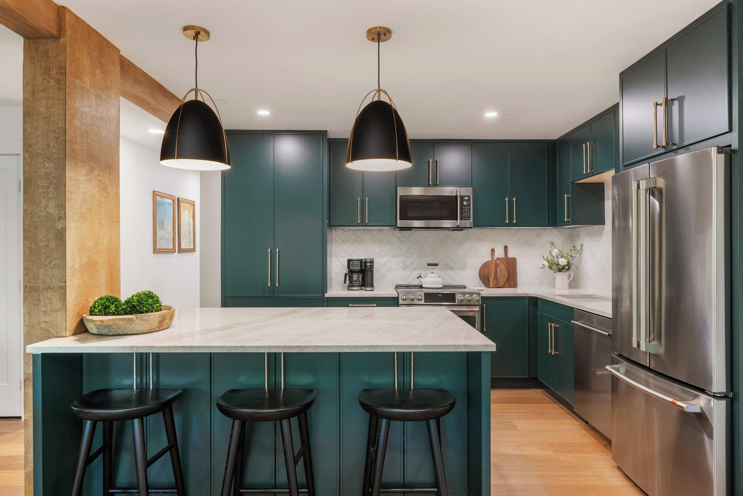 A modern kitchen with dark teal cabinets, a large island with bar stools, stainless steel appliances, and pendant lighting.