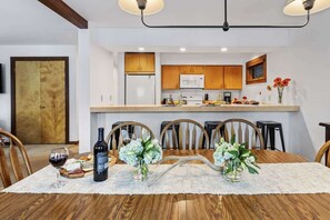 A dining area with a wooden table, chairs, a wine bottle, and flowers.
