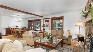 Sala de estar com sofá, mesa de centro e lareira. Há uma área de jantar com mesa e cadeiras.