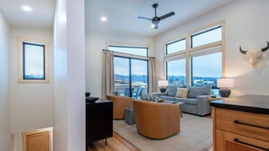 A spacious living room with large windows, a ceiling fan, and a bull skull decoration. - Teton Homestead: Scenic Loft Retreat (Driggs)