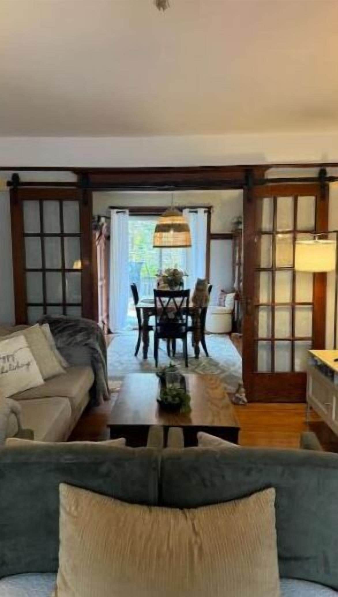 A living room with a sofa, a dining table with chairs, and a view through a glass door to an outdoor area.
