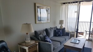 Un salon avec un canapé gris, deux tables d’appoint avec des lampes, une table basse en bois et un fauteuil en cuir noir.