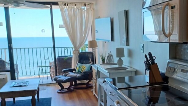 Une cuisine moderne dotée d’un grand îlot central, d’un coin repas avec une table et des chaises, et offrant une vue sur la mer grâce à une porte-fenêtre coulissante.