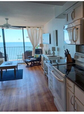 A modern kitchen with a large island, a dining area with a table and chairs, and a view of the sea through a sliding glass door.