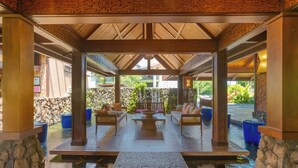 A covered outdoor seating area with wooden furniture and a stone wall backdrop.