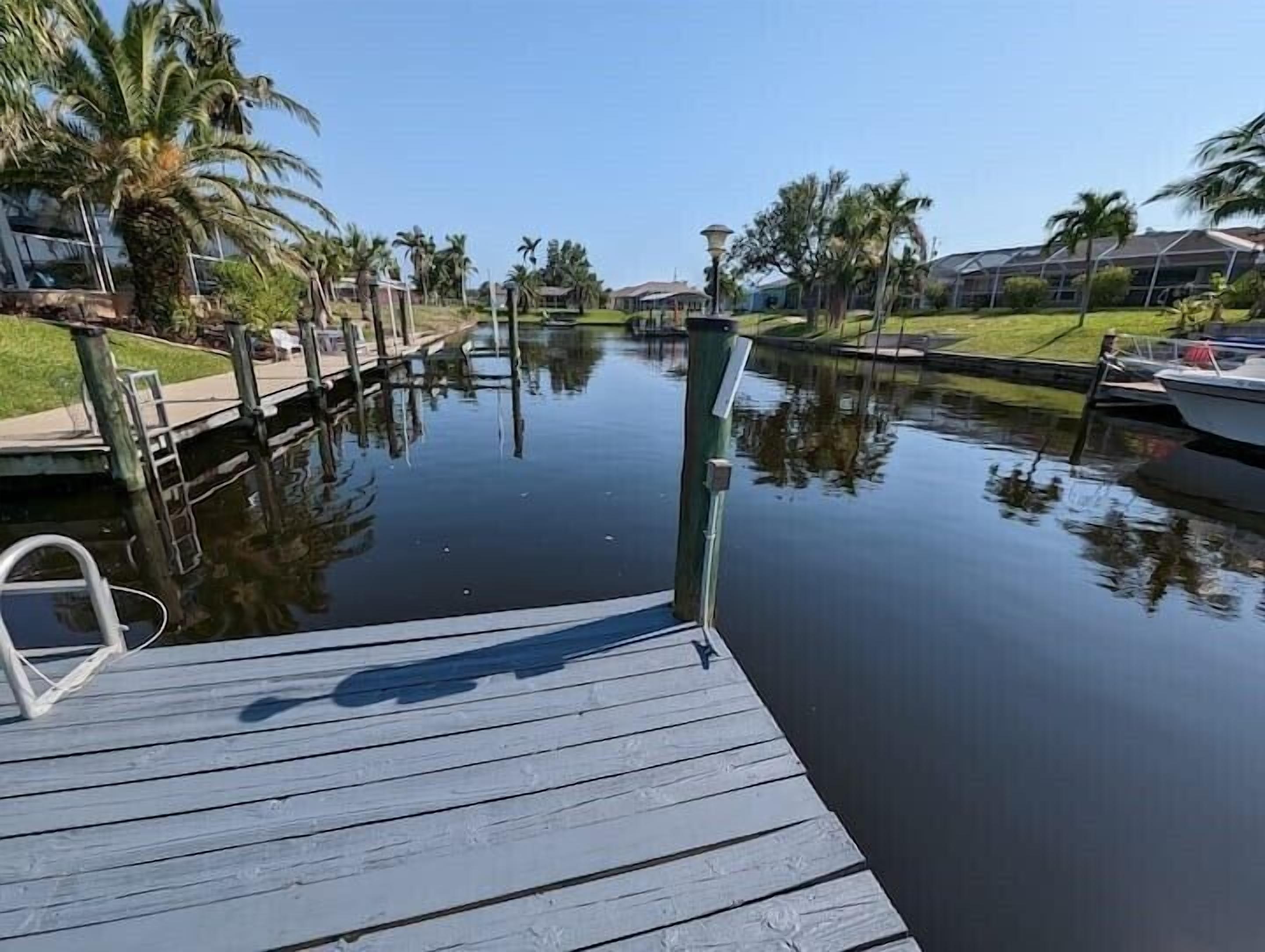 A calm waterway with a wooden dock, surrounded by palm trees and houses.