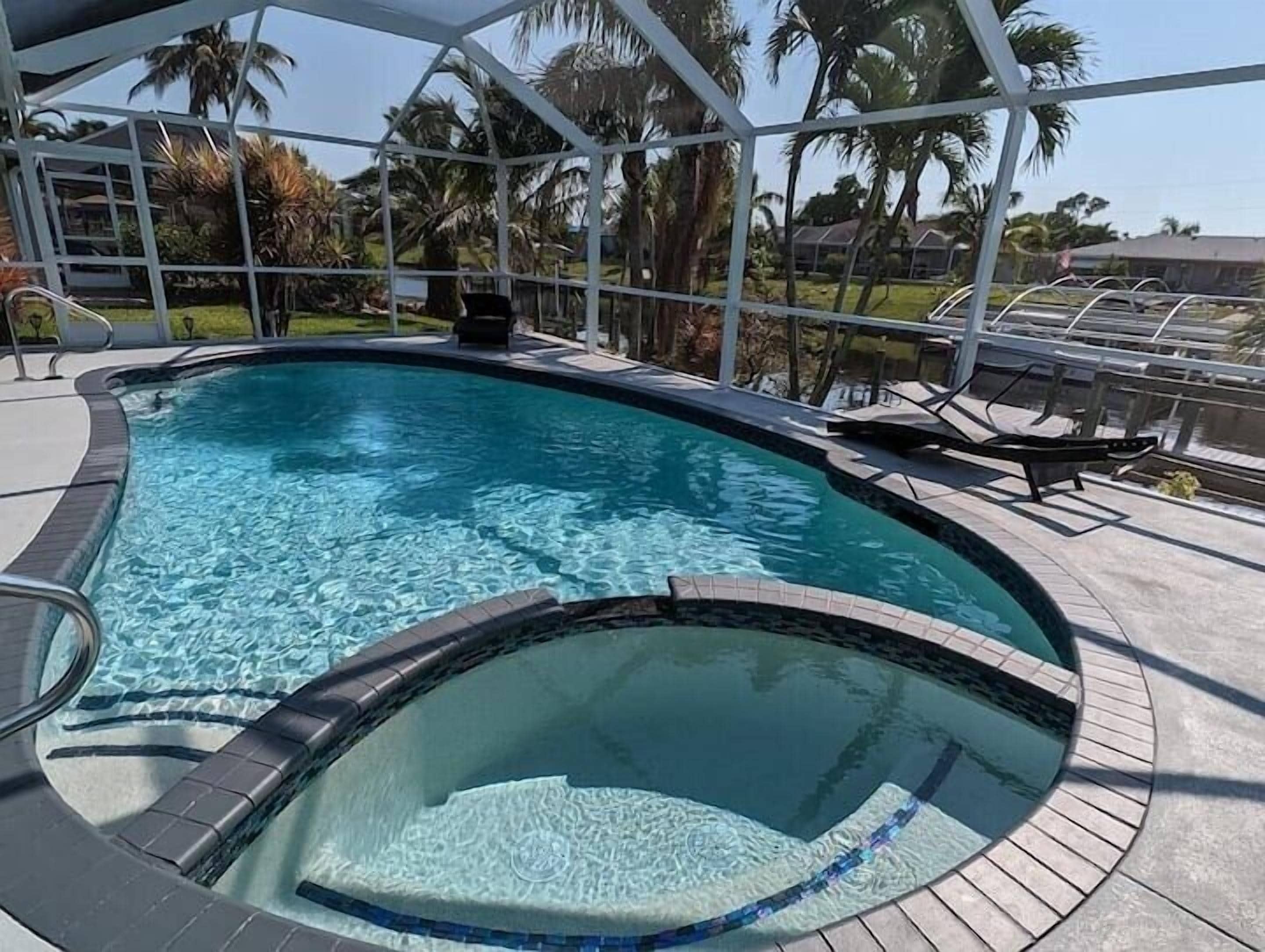 Una piscina con jacuzzi, rodeada por una zona techada con sillas y vistas a palmeras.