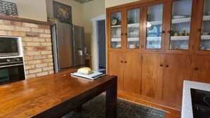 Une cuisine avec un mur en briques, une table en bois, une miche de pain, un meuble avec des portes en verre et un fourneau.