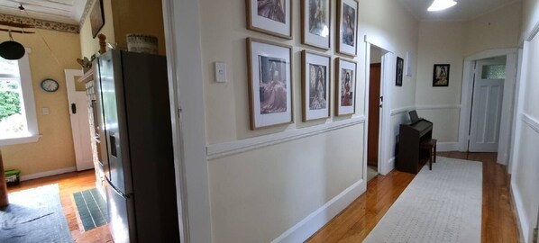 A hallway with a refrigerator, a clock, and framed pictures on the wall.