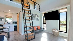 Amplia sala de estar con entrepiso, escalera, cocina y ventanas grandes que ofrecen vistas.