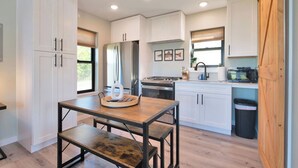 Una cocina moderna con armarios blancos, una mesa de comedor de madera y un cubo de basura negro.