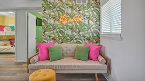 Ein Zimmer mit einer Couch, Kissen, einem Neon-Schild und einem Fenster mit Jalousien.