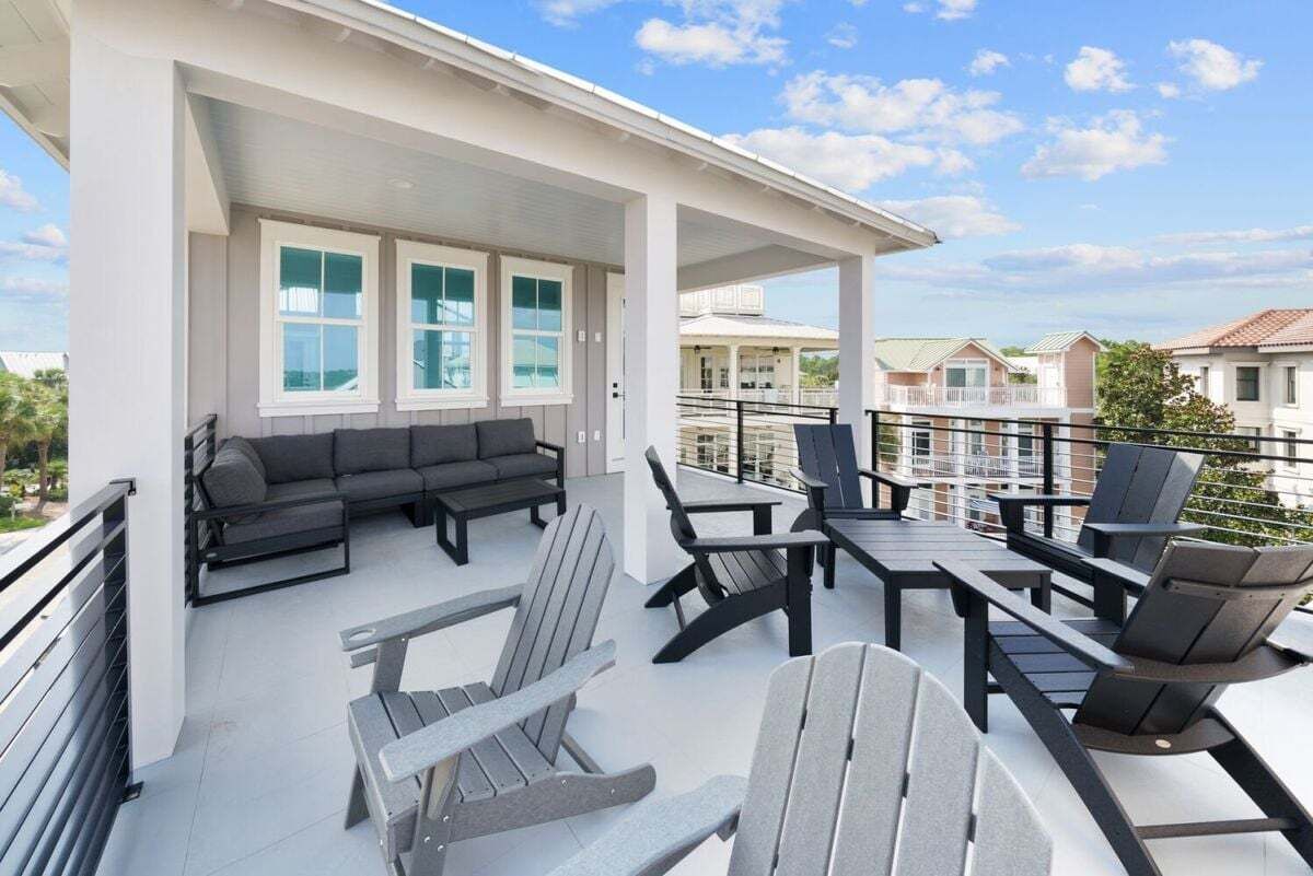 Un espacio exterior techado con sofás y sillones, una mesa y vistas a casas vecinas.