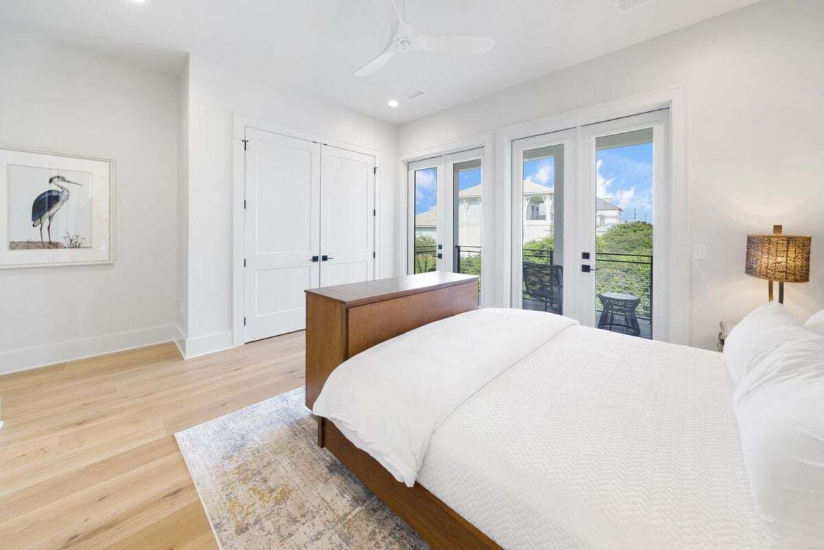 Quarto com uma cama grande, cômoda de madeira, ventilador de teto e vista para o exterior através de portas de vidro.