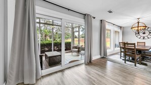 Ein geräumiges Zimmer mit großen Schiebegläsern, die zu einem Garten führen, einem Essbereich mit Holzmöbeln und einer modernen Chandelüster.