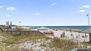 Ein Strand mit einer Holzpromenade, Strandsonnenschirmen und einem sandigen Bereich mit Booten.