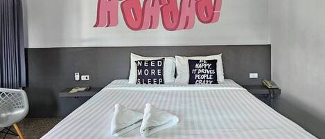 Habitación de hotel con una cama grande, dos mesitas de noche, una silla y una pared con citas motivacionales.