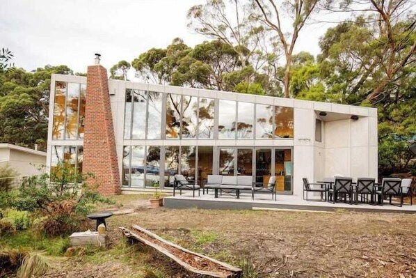 A modern building with large glass windows, a brick chimney, and outdoor seating. - The Beach House at Great Bay (Great Bay)