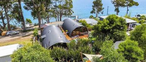A modern eco-friendly building with cylindrical structures, surrounded by lush greenery and overlooking a body of water.