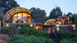 A modern, dome-shaped building with a glass facade, surrounded by lush greenery and a stone wall. - Sanctuary Bruny Island - 2 Domes (Adventure Bay)