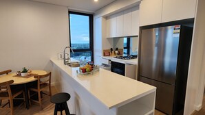 Una cucina moderna con un piano di lavoro bianco, elettrodomestici in acciaio inossidabile e vista sulla città attraverso un'ampia finestra.
