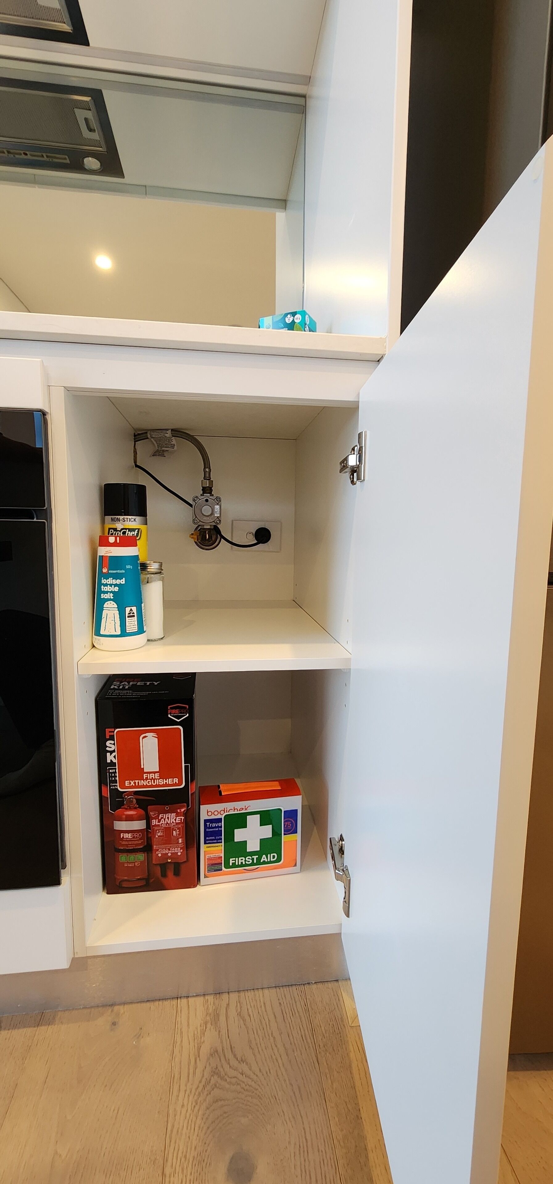 Een keuken met een inbouwfornuis, een spoelbak en een plank met een brandblusser, verbanddoos en zoutcontainer.