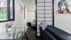 Ett modernt rum med ett glasbord, en svart lädersoffa, en skjutbar shoji-skärm och konstverk på väggarna.