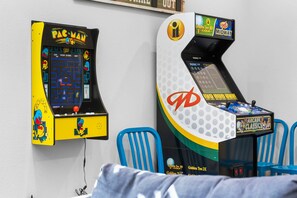 Two arcade machines, one labeled 'PAC-MAN' and the other 'MIDWAY,' in a room with blue chairs. - Water View Retreat with Arcades, Private Hot Tub, Community Pools, Dog Park & Free Daily Tickets (Hollister)
