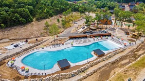 Ein großer Pool im Freien mit einer umlaufenden Liegefläche, Liegestühlen und Sonnenschirmen.