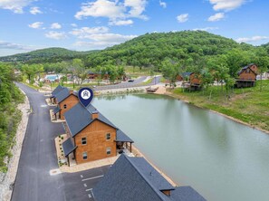 A riverside hotel with a parking lot, a swimming pool, and a view of the surrounding forest.
