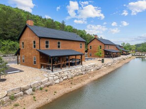 A wooden cabin with a stone foundation, a covered outdoor seating area, and a view of a calm lake.