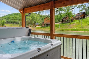 A hot tub on a wooden deck with a view of a river and houses in the background.
