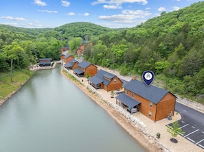 A row of wooden cabins by a lake with a stone walkway, surrounded by forest.