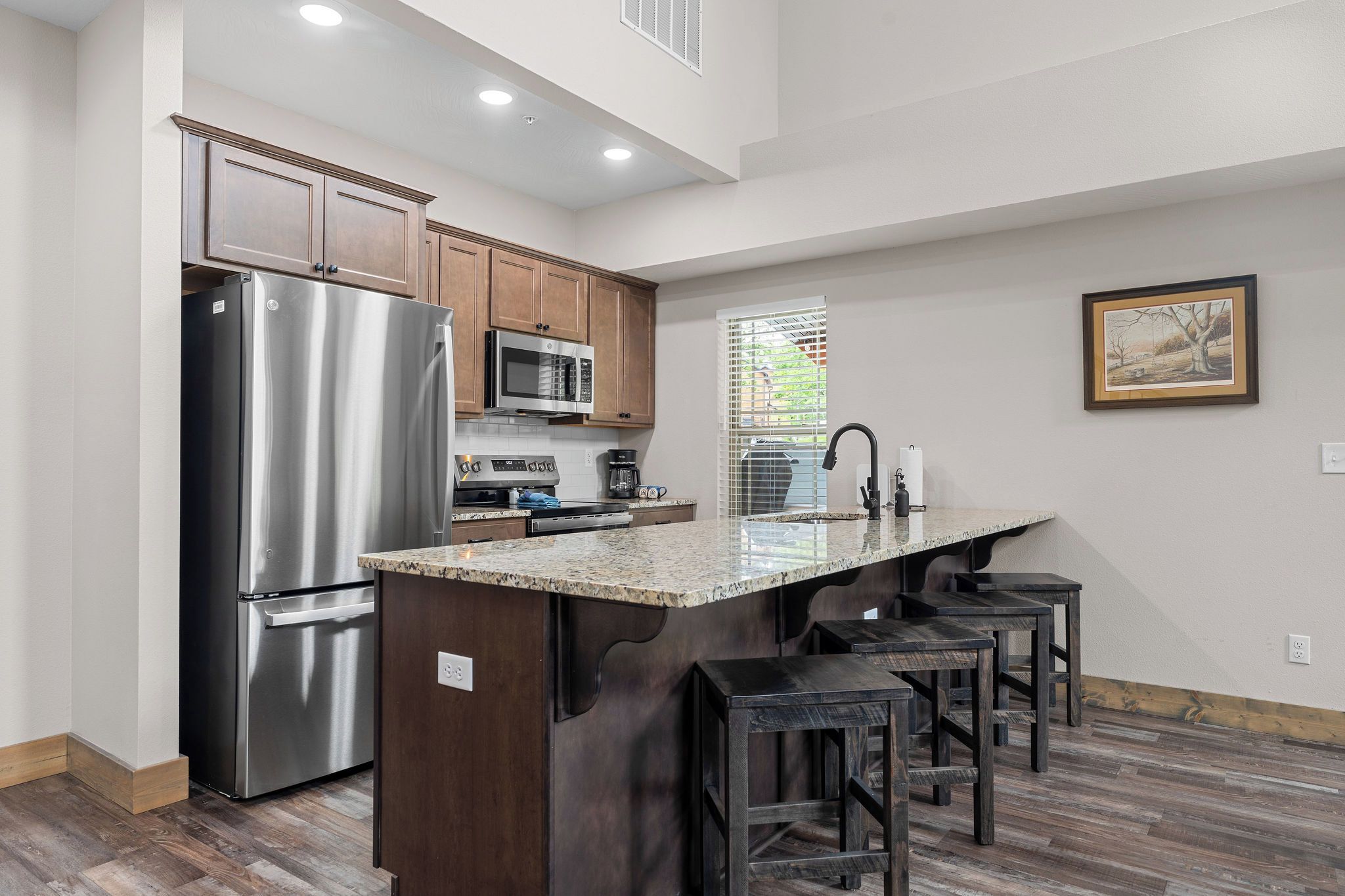 A modern kitchen with stainless steel appliances, a granite countertop, and a bar stool area.