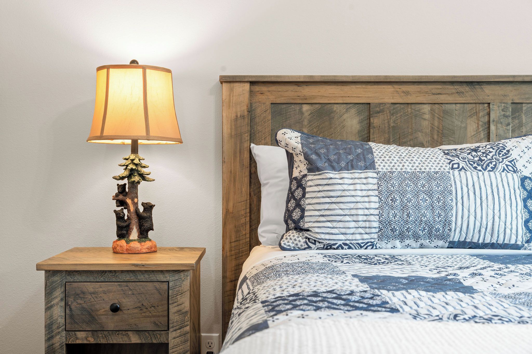 A bedroom with a wooden headboard, a nightstand with a lamp, and a bed with patterned bedding.