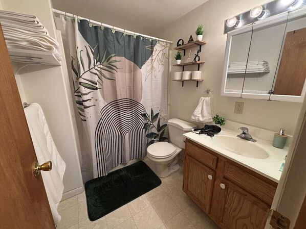 A bathroom with a shower curtain, toilet, sink, and wooden cabinets.