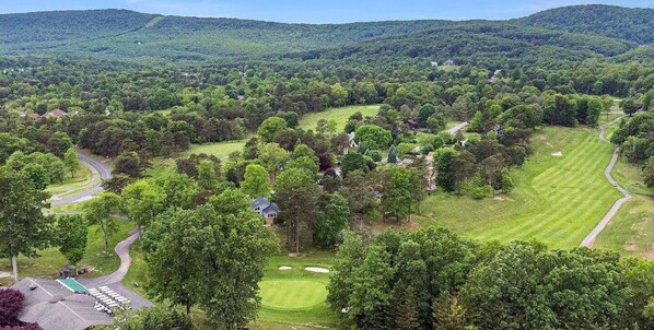A golf course with multiple holes, surrounded by dense forest and rolling hills.