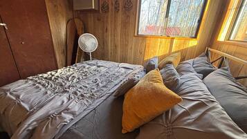 A cozy room with a bed, a fan, and a window with a view of trees.